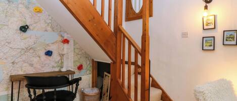 A wooden staircase, a map on the wall, a desk with a chair, and a fluffy white chair.