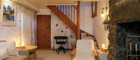 A cozy living room with a stone fireplace, a wooden staircase, a map on the wall, and a sofa.