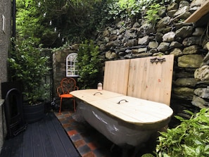 A bathtub in a rustic outdoor setting with a stone wall, a wooden door, and a chair. - Waterfall Retreat (Blaenau Ffestiniog)