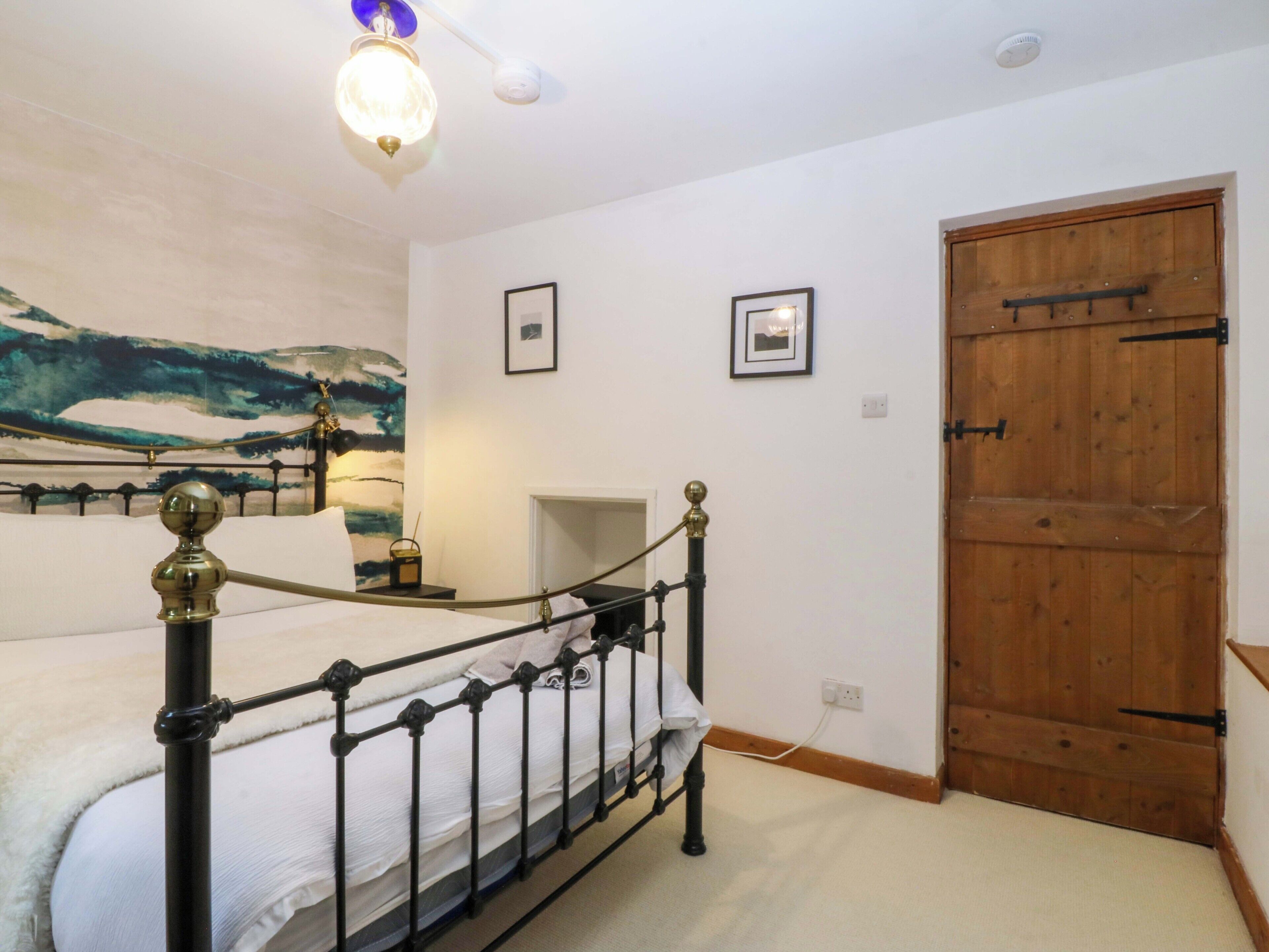 Une chambre à coucher avec un lit, une porte en bois, un tableau accroché au mur et un luminaire au plafond.