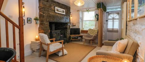 A cozy living room with a stone fireplace, wooden furniture, and a woven coffee table.