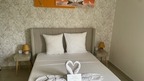 Habitación de hotel con cama, dos mesitas de noche, un papel tapiz floral en la pared y una disposición de toallas en forma de corazón sobre la cama.
