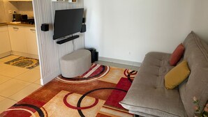 Una sala de estar con sofá, reposapiés y televisor de pantalla plana montado en la pared.