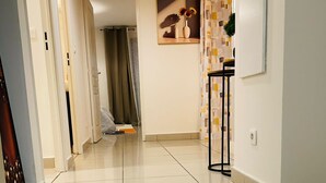Un pasillo limpio y bien iluminado con un letrero que dice 'BIENVENUE' en el suelo, que conduce a una habitación con un cuadro y una cortina estampada.