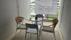 Un balcón con una mesa redonda y cuatro sillas, una planta en maceta y vistas a edificios.