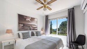A bedroom with a bed, a nightstand, a chair, a ceiling fan, a large window with curtains, and a painting on the wall. - Spectacular flat, ideal for family holidays – Monte Miraflores (AN)