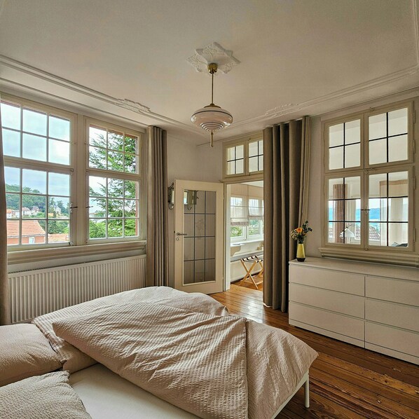 Une chambre à coucher avec un lit, une commode, un radiateur et de grandes fenêtres.