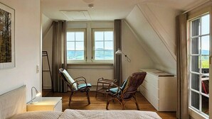 Una camera da letto con un letto grande, due poltrone in vimini, un tavolino e vista mare attraverso ampie finestre.
