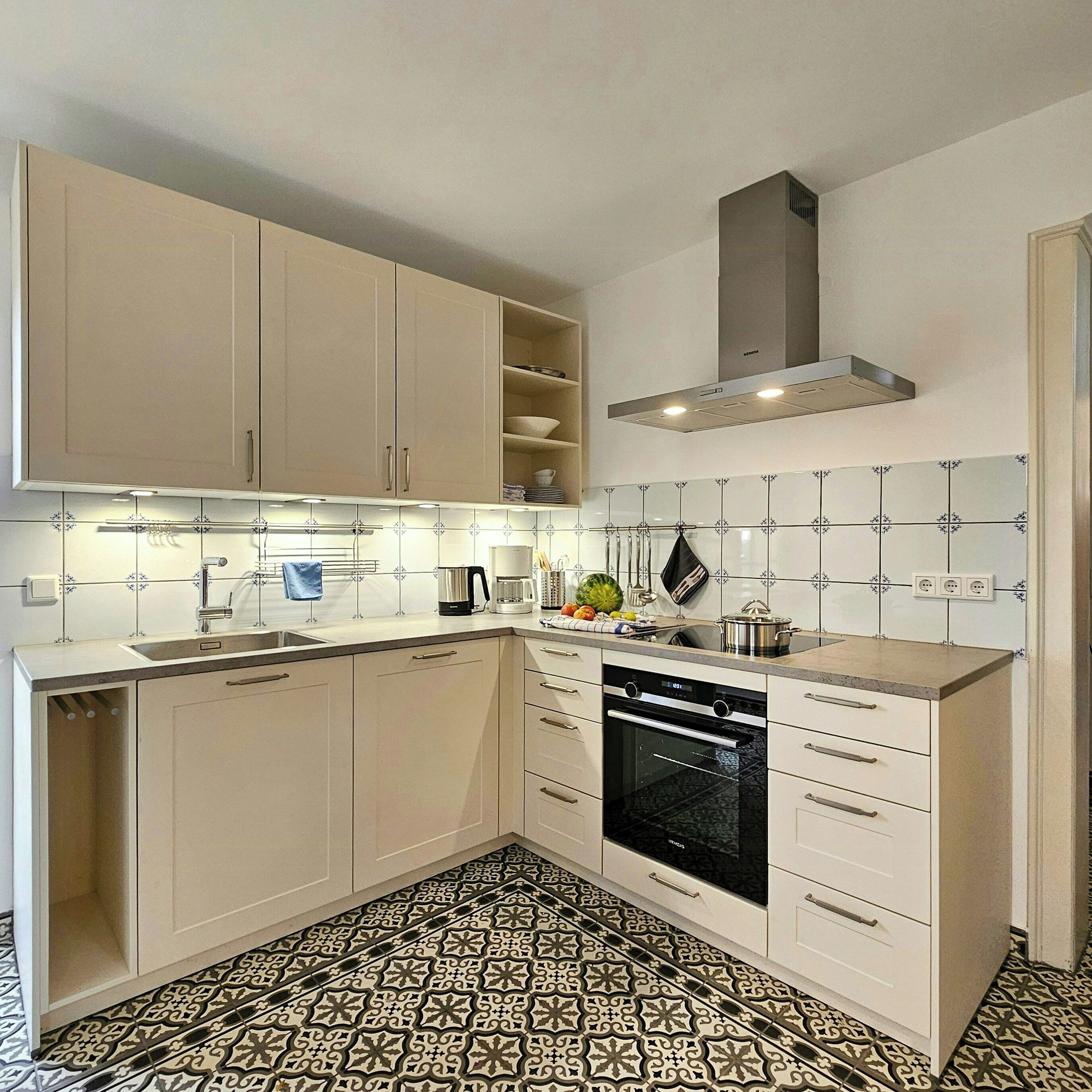 A modern kitchen with white cabinets, a built-in oven, and patterned floor tiles.