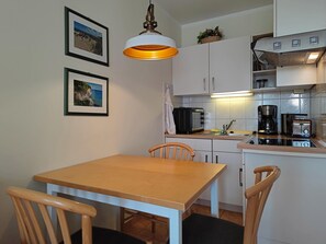 A compact kitchen with a dining table, chairs, a hanging light fixture, and a coffee maker. - Seepark Sellin Ferienwohnung Nahe Strand (Sellin)