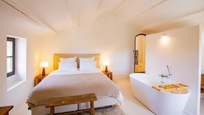 Una camera da letto con un letto, lampade da comodino, una panca in legno, una vasca e uno specchio.
