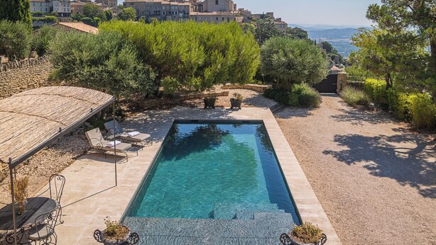 Una piscina rettangolare con acqua cristallina, circondata da un’area ghiaiata, con lettini e un tavolo.