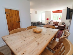 Un comedor con una mesa de madera, sillas y un tazón. Se ve un sofá y una televisión al fondo.