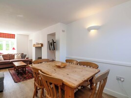 Un comedor con una mesa y sillas de madera, un sofá, un televisor en la pared y una ventana con persianas.
