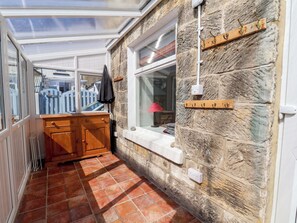 A narrow corridor with a stone wall, a wooden bench, a window, and a coat rack. - Cozy Cottage (Saltburn-by-the-Sea)