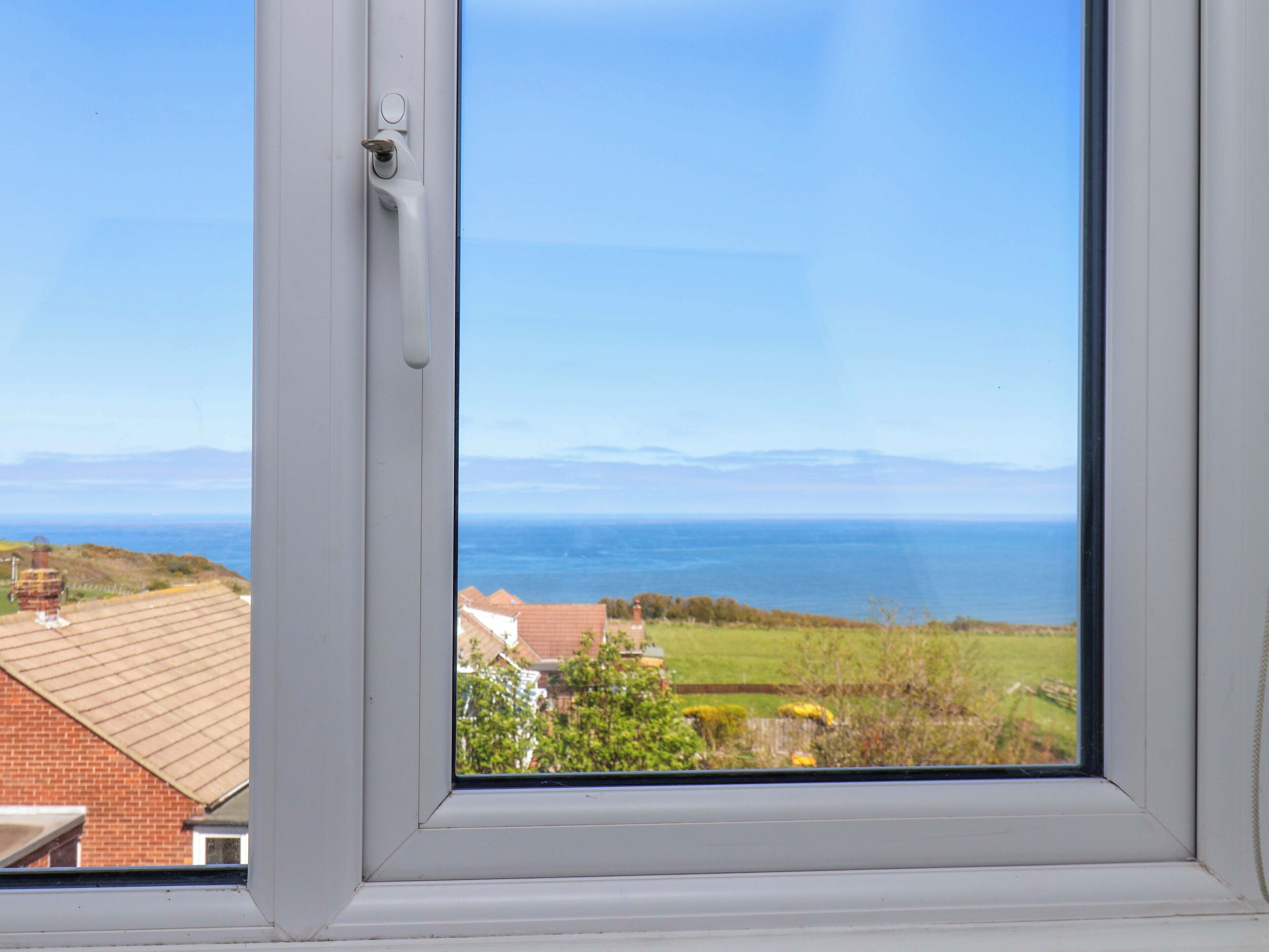 Una ventana con vista al mar, un área verde y un edificio de techo rojo.