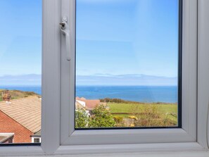 Ein Fenster mit Meerblick, eine Rasenfläche und ein Gebäude mit rotem Dach.