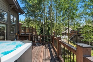 Een houten terras met een jacuzzi, omgeven door bomen en een gebouw.