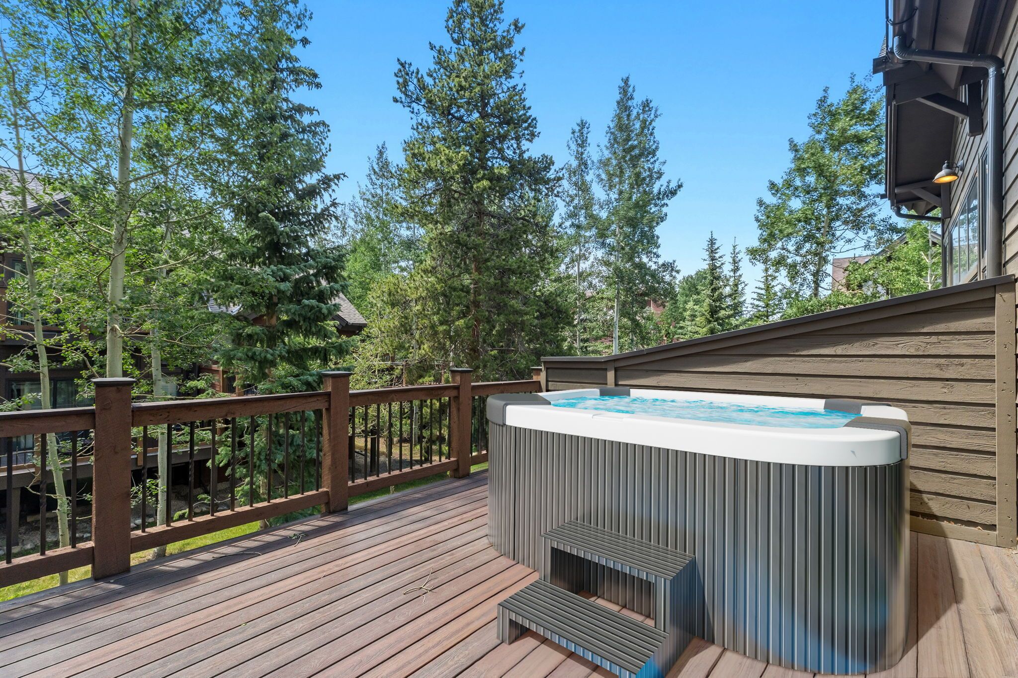 Una terraza de madera con un jacuzzi, rodeada de árboles y un edificio.