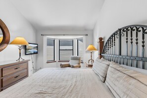 Een slaapkamer met een bed, twee nachtkastjes met lampen, een stoel, een dressoir, een televisie en een raam met jaloezieën.
