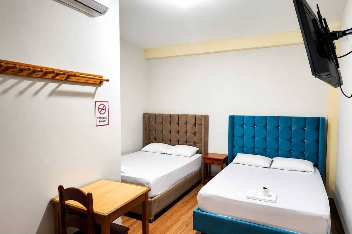 A hotel room with two beds, a desk, a chair, a TV mounted on the wall, and a no-smoking sign.