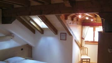 A bedroom with a sloped ceiling, a bed, a chair, and a window with curtains.