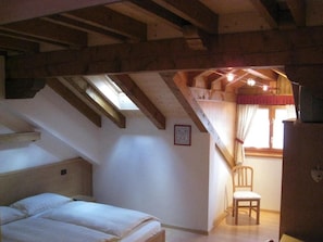 A bedroom with a sloped ceiling, a bed, a chair, and a window with curtains. - Affittacamere Alle Trote (SÙTRIO)