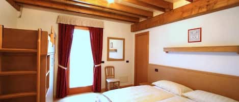 Une chambre à coucher avec un lit en bois, une chaise, une étagère et une fenêtre avec des rideaux.