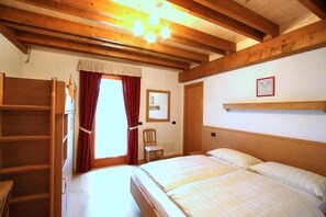 A bedroom with a wooden bed, a chair, a shelf, and a window with curtains. - Affittacamere Alle Trote (SÙTRIO)