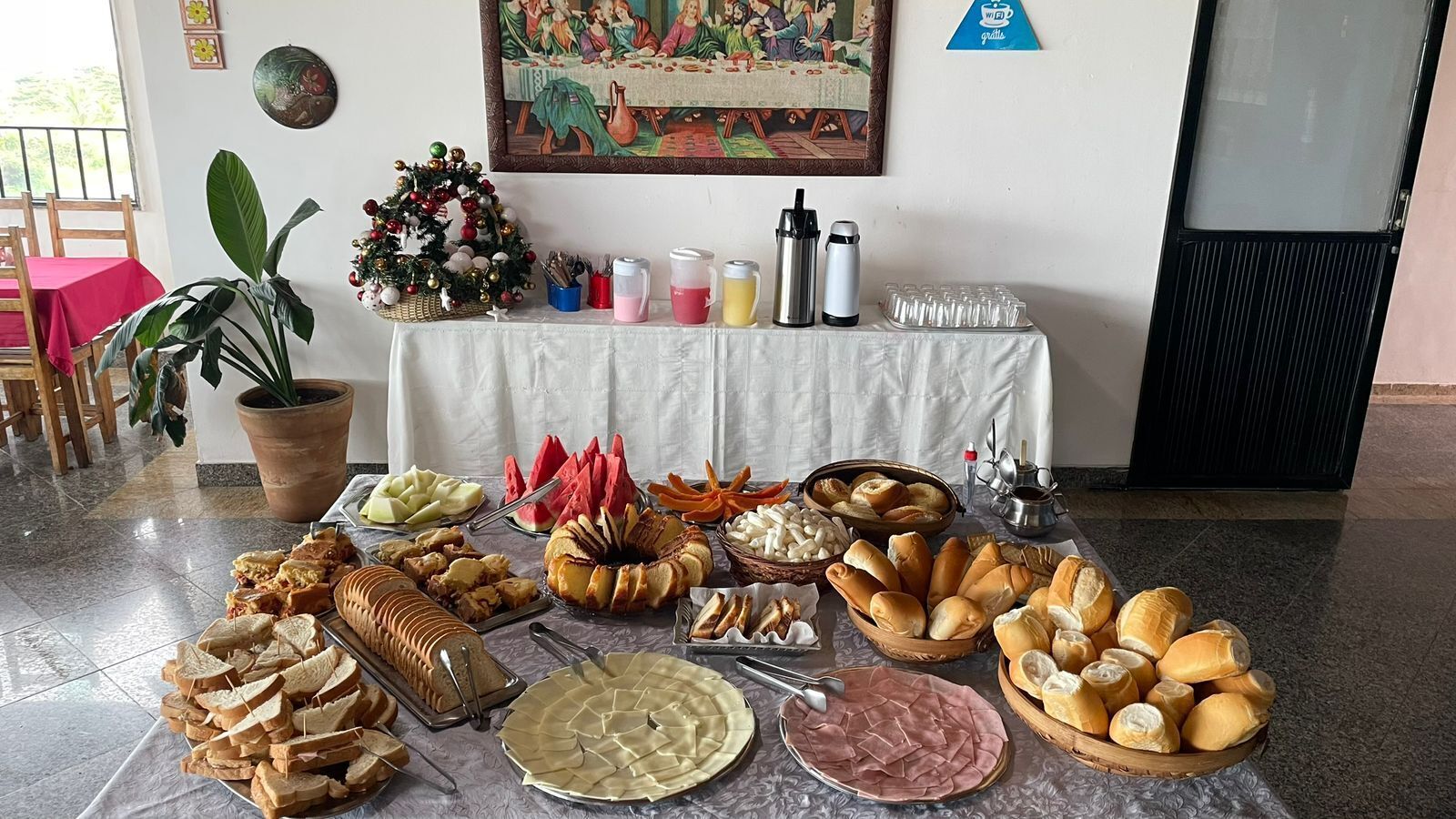 Uma mesa de buffet com diversos alimentos, uma guirlanda de Natal e um quadro na parede.