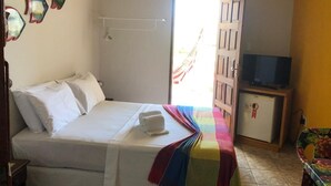 Une chambre à coucher avec un lit, une télévision, un réfrigérateur et une fenêtre avec des rideaux.