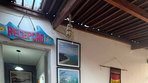 Un espace d’accueil avec un panneau indicateur, des tableaux encadrés, une plante en pot, une table en bois et un tapis bleu.