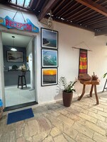 Uma área de recepção com uma placa, quadros emoldurados, um vaso de planta, uma mesa de madeira e um tapete azul.
