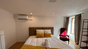 Ein Hotelzimmer mit einem Bett, einem roten Sessel, einem Fenster mit Vorhängen und einer Klimaanlage.