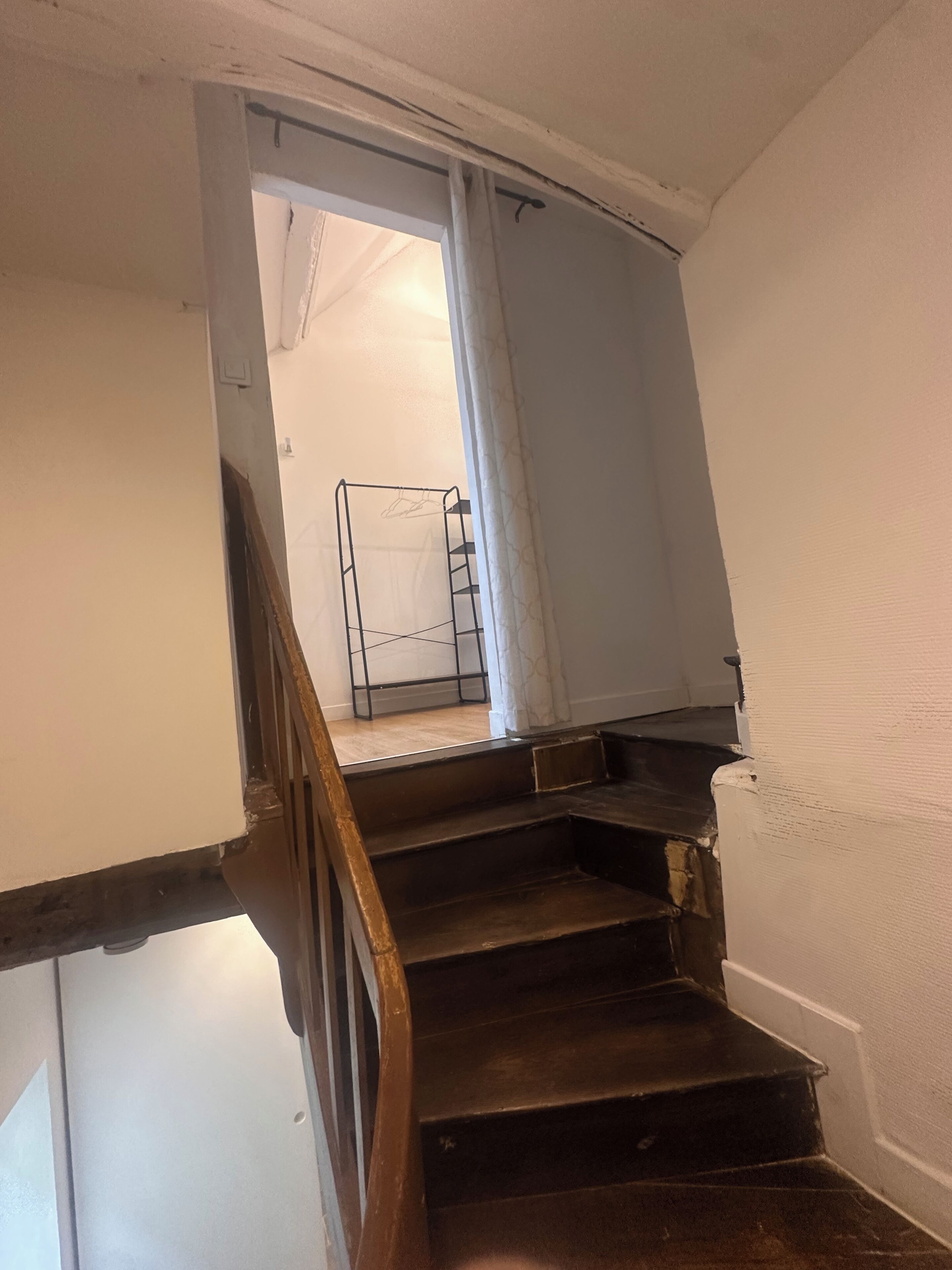 A staircase with a wooden handrail, a metal banister, and a white wall.