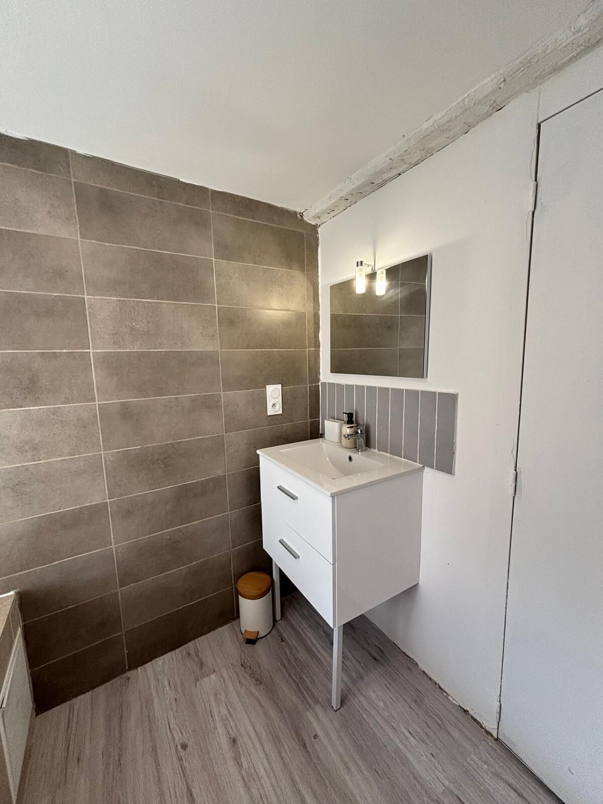 Ein Badezimmer mit einem weißen Waschbecken, einem Spiegel und einer gefliesten Wand.
