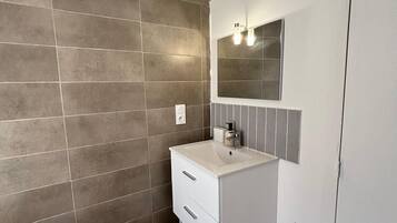 Ein Badezimmer mit einem weißen Waschbecken, einem Spiegel und einer gefliesten Wand.