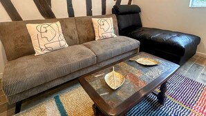Ein Wohnzimmer mit gestreifter Wand, einem Sofa mit gemusterten Kissen, einem Couchtisch und einem schwarzen Ledersessel.