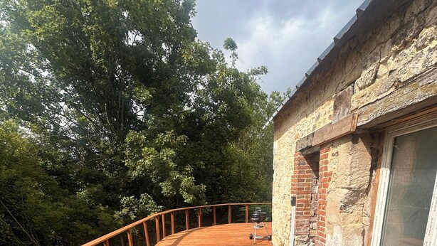 Eine Holzterrasse mit Grill, Steinmauer und Fenster.