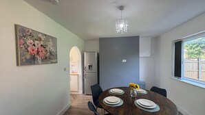 Un comedor con una mesa redonda dispuesta para cuatro personas, sillas alrededor, un jarrón con girasoles, un cuadro en la pared y una ventana con vistas.