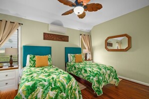 A room with two beds, a ceiling fan, a wall-mounted air conditioner, a mirror, and a window with curtains. - Kauai Lae Nani 233 2 Bedroom Condo (Kapaa)