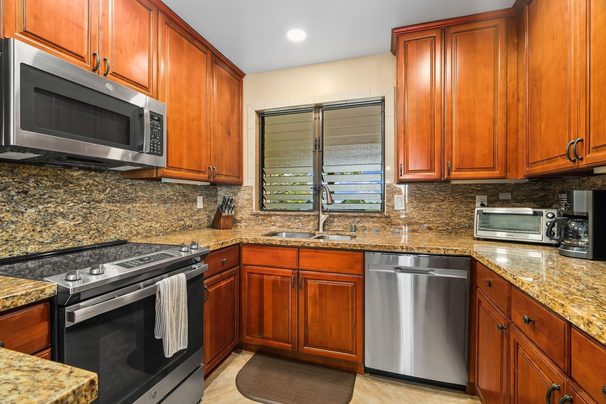 A kitchen with granite countertops, stainless steel appliances, wooden cabinets, and a dishwasher.