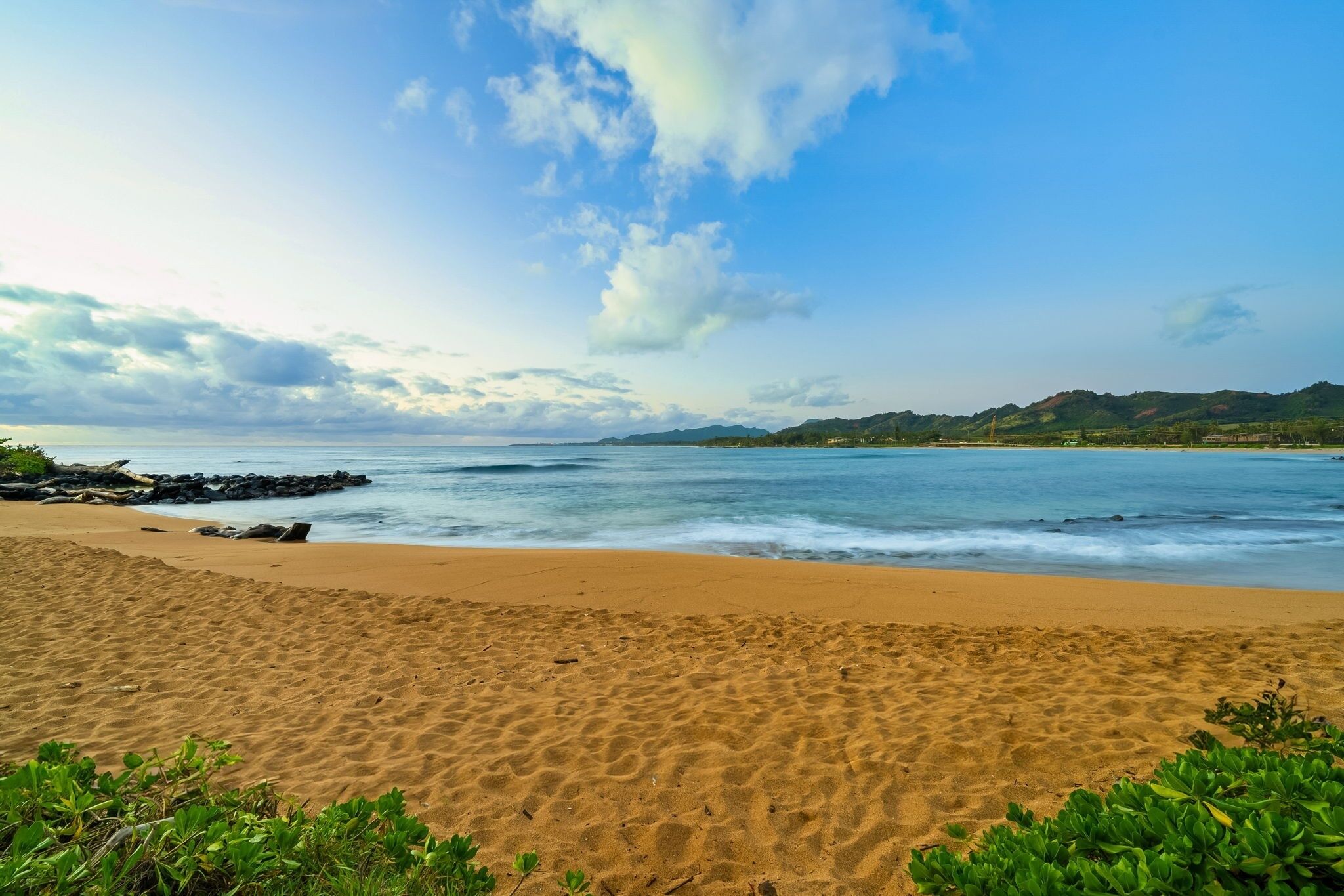 A beach with a sandy shore, waves, and distant hills.