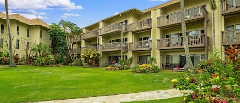 Un hotel de varios pisos con balcones, un césped bien cuidado y jardines tropicales.