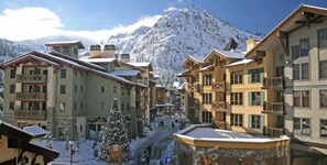 Un pueblo cubierto de nieve en la montaña, con edificios de varios pisos, una calle principal y un gran árbol de Navidad.