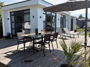 Een modern terras buiten, met een houten terras, een eettafel met stoelen, en lounge fauteuils.