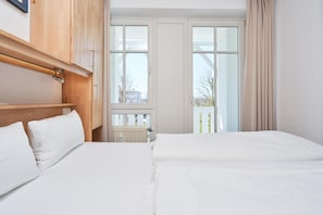 Une chambre d’hôtel avec deux lits, une tête de lit en bois, une fenêtre donnant sur un paysage agréable et un radiateur.