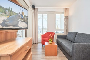 Un salon avec un téléviseur, un fauteuil rouge, un canapé gris et une table basse en bois.