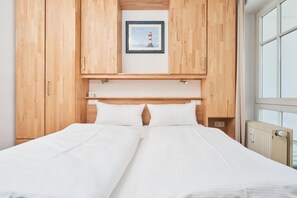 Ein Doppelbett mit weißen Leinentüchern, einem hölzernen Kopfteil und einem gerahmten Bild eines Leuchtturms.
