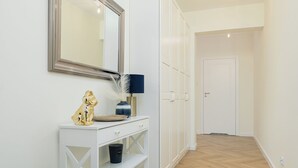A hallway with a white console table, a mirror, a blue lamp, a gold dog figurine, and a white wardrobe.